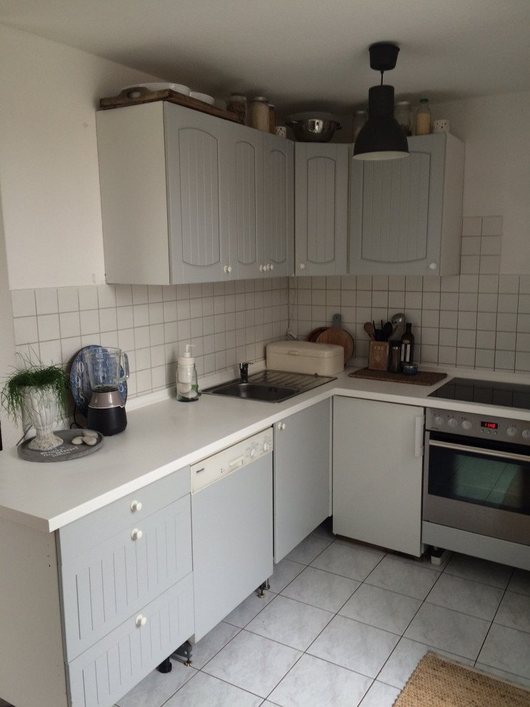 Small rural grey and white l-shaped open plan kitchen in Berlin with a single-bowl sink, beaded cabinets, grey cabinets, laminate countertops, white splashback, ceramic splashback, stainless steel appliances, ceramic flooring, no island, grey floors, white worktops and a wallpapered ceiling.