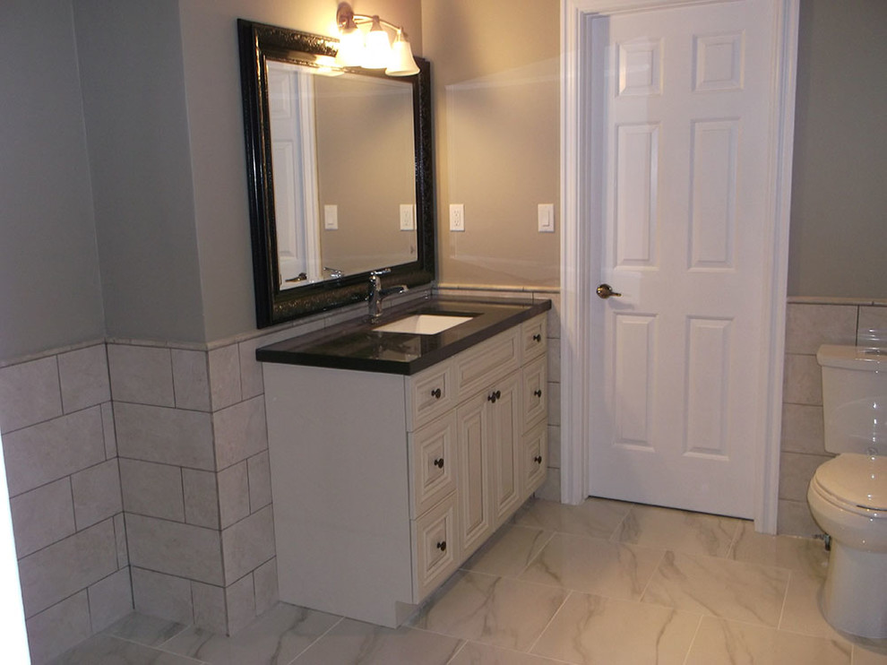 Inspiration for a mid-sized transitional gray tile and ceramic tile ceramic tile and gray floor bathroom remodel in Toronto with raised-panel cabinets, white cabinets, a two-piece toilet, gray walls, an undermount sink and solid surface countertops