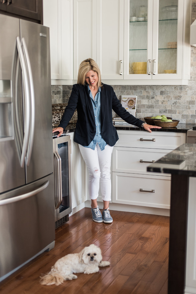 Inspiration for a transitional medium tone wood floor and brown floor kitchen remodel in Toronto with an undermount sink, recessed-panel cabinets, white cabinets, granite countertops, gray backsplash, travertine backsplash, stainless steel appliances and an island