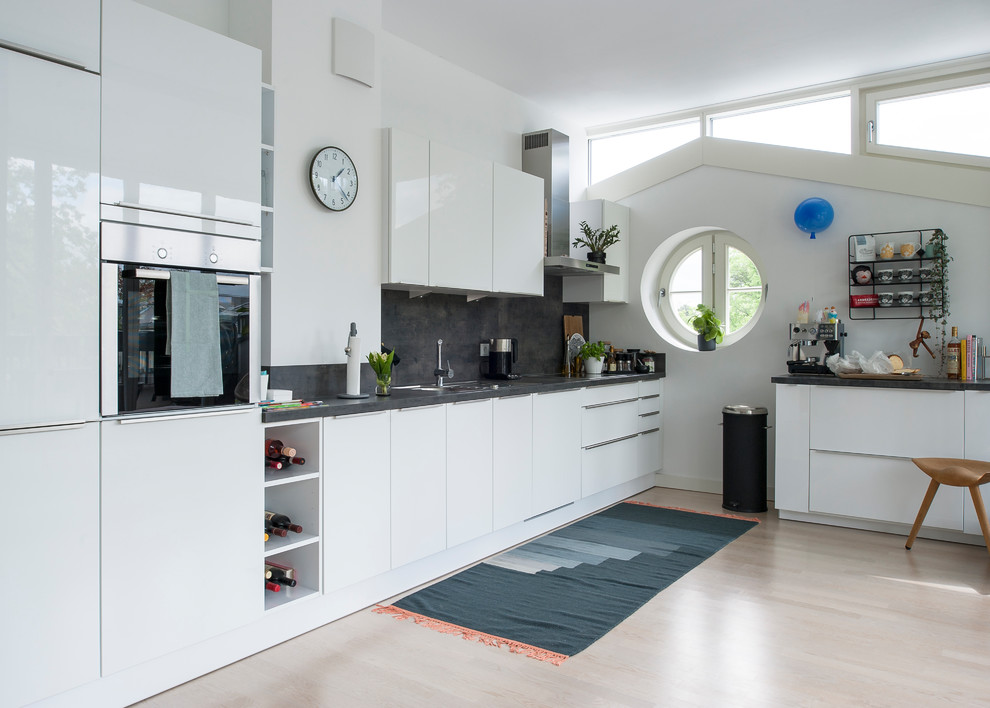 This is an example of a mid-sized contemporary single-wall kitchen in Berlin with flat-panel cabinets, stainless steel appliances, light hardwood floors, white cabinets, grey splashback, with island and beige floor.