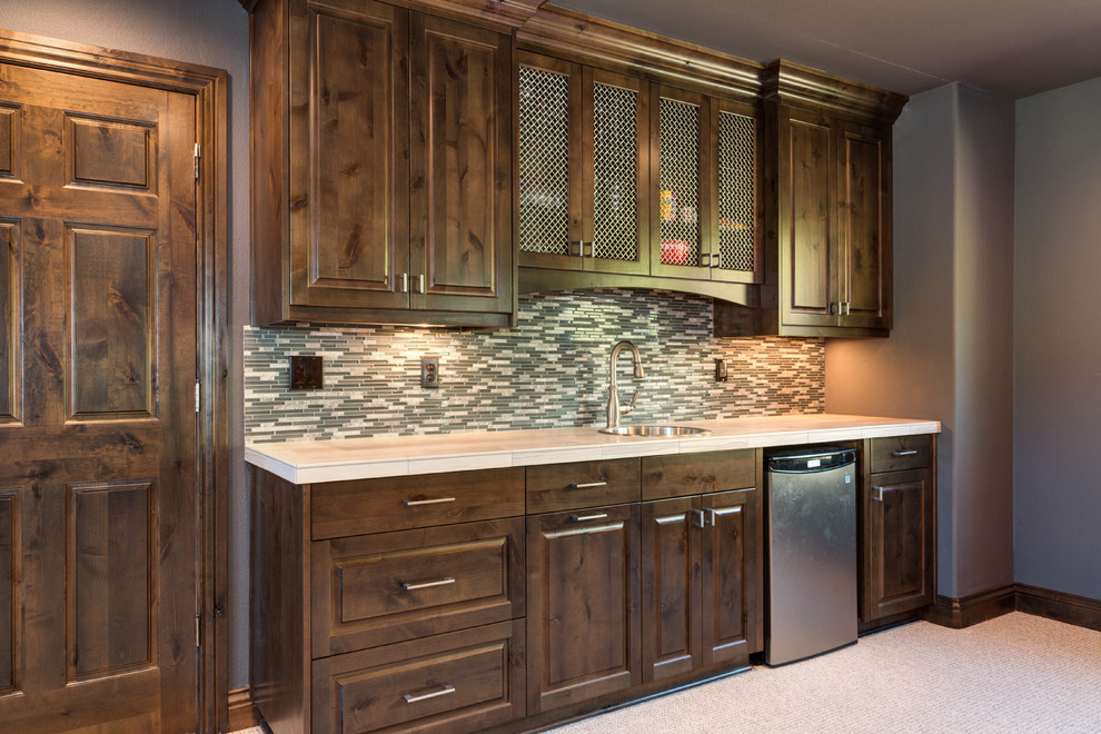 Photo of a large country galley wet bar in Portland with a drop-in sink, raised-panel cabinets, dark wood cabinets, green splashback, matchstick tile splashback and carpet.