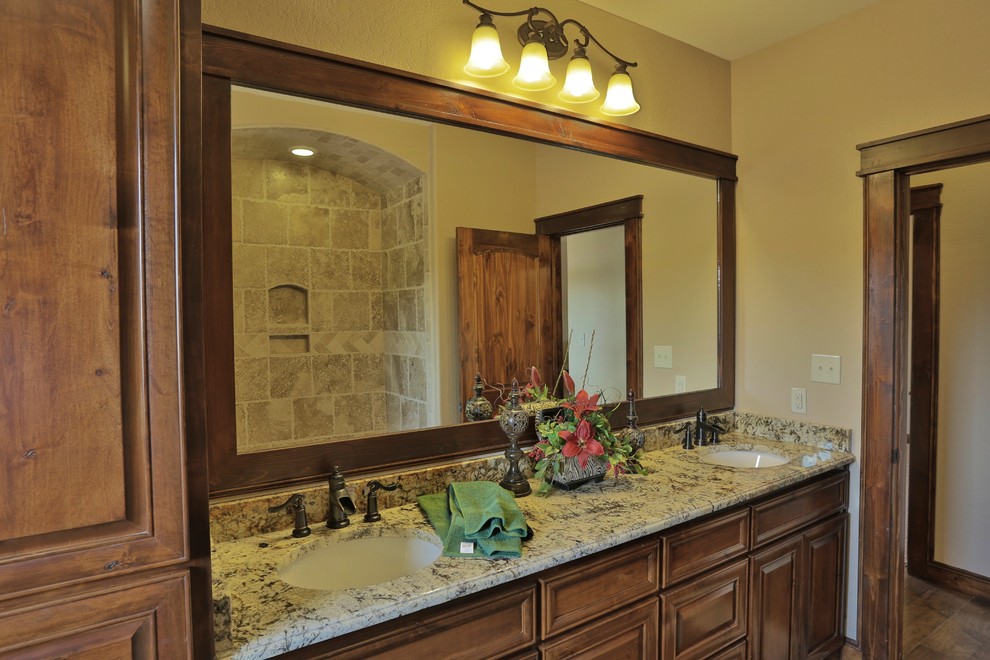 Design ideas for a small mediterranean bathroom in Dallas with an undermount sink, raised-panel cabinets, dark wood cabinets, granite benchtops, an alcove tub, a shower/bathtub combo, a two-piece toilet, brown tile, stone tile, beige walls and travertine floors.
