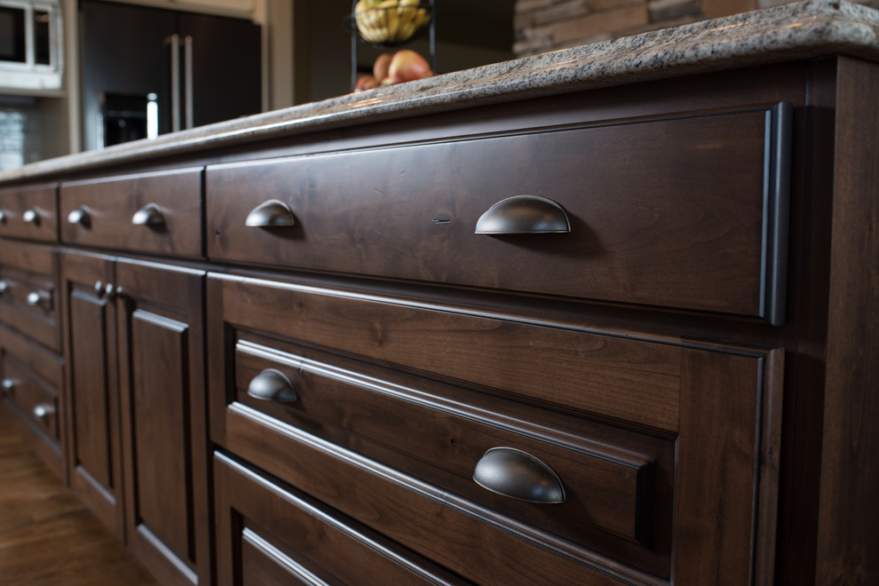 Inspiration for a large rustic l-shaped dark wood floor and brown floor eat-in kitchen remodel with a farmhouse sink, raised-panel cabinets, dark wood cabinets, granite countertops, gray backsplash, ceramic backsplash, black appliances and an island