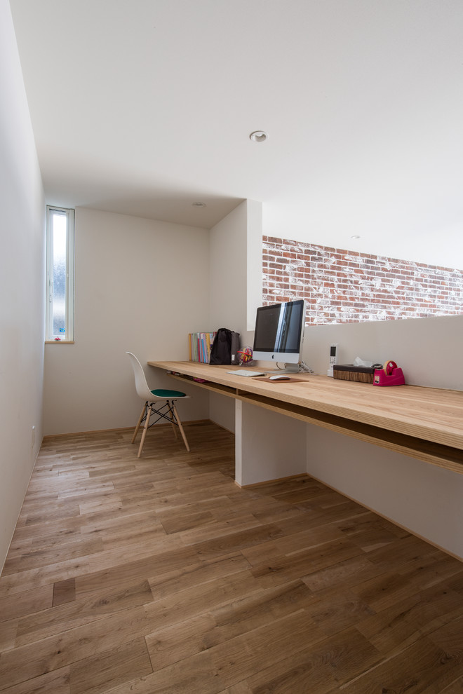 This is an example of a small modern home office in Kyoto with white walls, light hardwood floors, a built-in desk and beige floor.