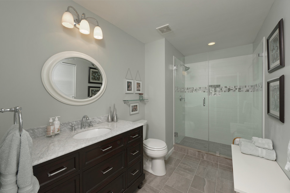 Photo of a mid-sized traditional master bathroom in DC Metro with recessed-panel cabinets, dark wood cabinets, an alcove shower, a two-piece toilet, multi-coloured tile, ceramic tile, grey walls, ceramic floors, an undermount sink, marble benchtops and grey floor.