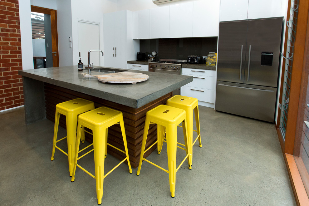 This is an example of a mid-sized industrial galley eat-in kitchen in Brisbane with an undermount sink, flat-panel cabinets, white cabinets, concrete benchtops, grey splashback, glass sheet splashback, stainless steel appliances, concrete floors and with island.