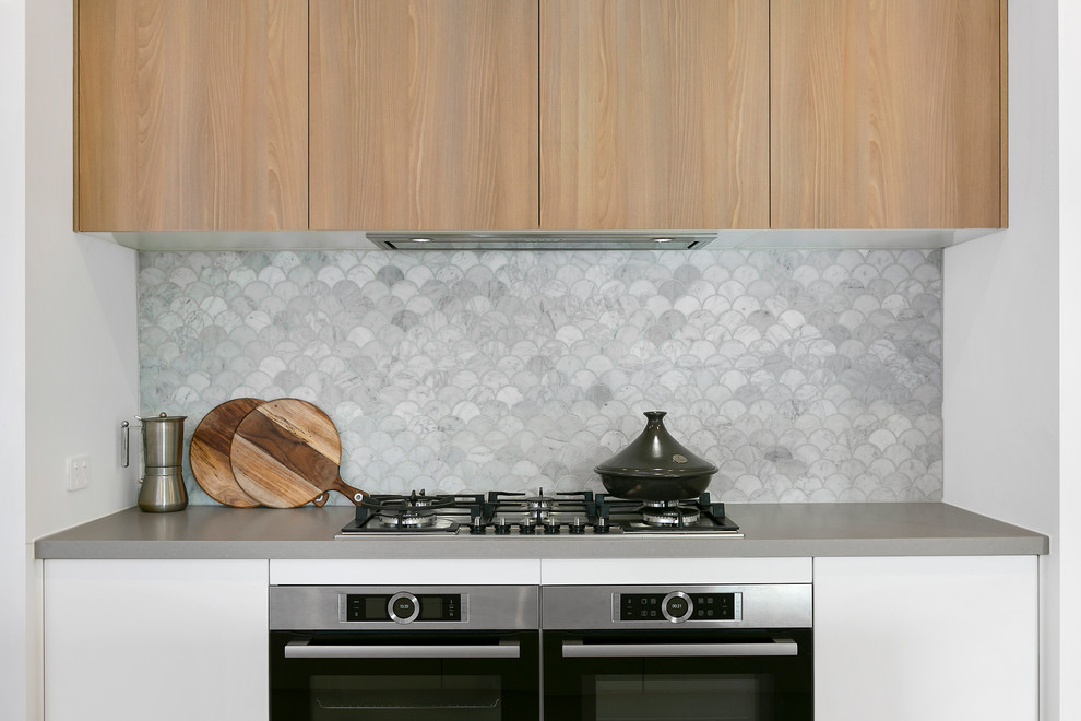 Inspiration for a contemporary u-shaped open plan kitchen in Melbourne with an undermount sink, flat-panel cabinets, white cabinets, quartz benchtops, grey splashback, stone tile splashback, stainless steel appliances, medium hardwood floors, with island and grey benchtop.