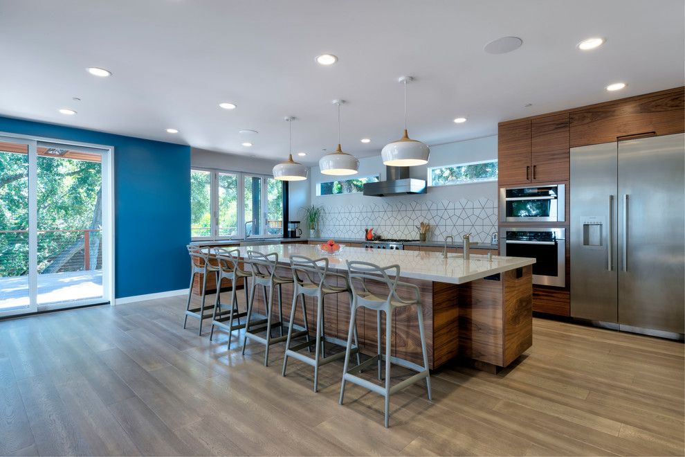 Photo of a large contemporary l-shaped kitchen in San Francisco with a drop-in sink, white splashback, stainless steel appliances, light hardwood floors, with island, beige floor, grey benchtop, flat-panel cabinets, dark wood cabinets, solid surface benchtops and ceramic splashback.