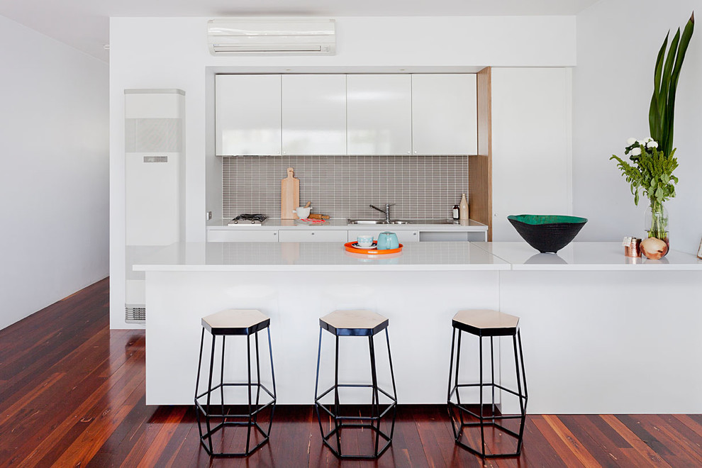 Inspiration for a contemporary galley kitchen in Melbourne with a drop-in sink, flat-panel cabinets, white cabinets, grey splashback, dark hardwood floors and a peninsula.