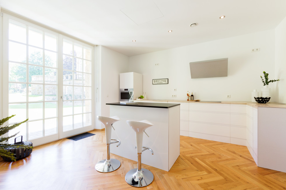 This is an example of a contemporary l-shaped kitchen in Essen with flat-panel cabinets, white cabinets, medium hardwood floors, with island, brown floor and beige benchtop.