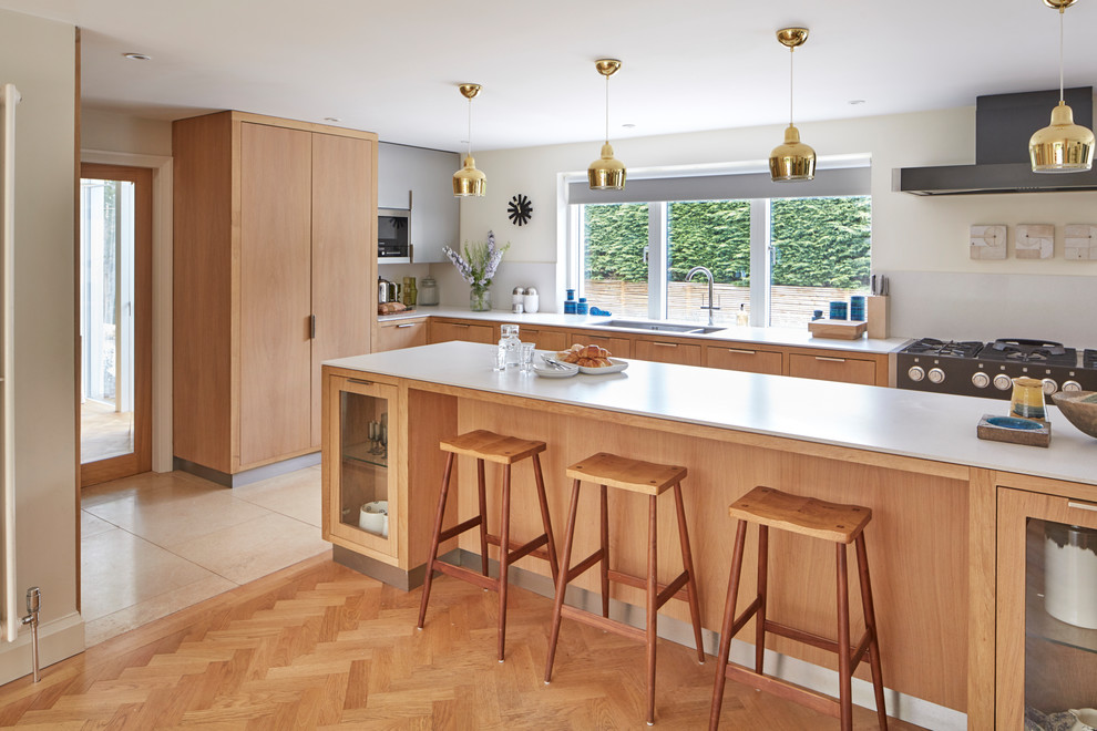 This is an example of a mid-sized transitional l-shaped open plan kitchen in Berkshire with flat-panel cabinets, brown cabinets, grey splashback, black appliances, medium hardwood floors, with island and brown floor.