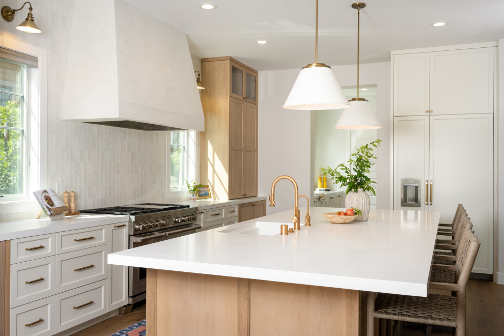 Photo of a large transitional l-shaped open plan kitchen in San Francisco with an undermount sink, shaker cabinets, light wood cabinets, quartz benchtops, white splashback, ceramic splashback, panelled appliances, light hardwood floors, with island, brown floor and white benchtop.