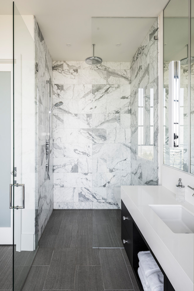 This is an example of a large contemporary master bathroom with flat-panel cabinets, black cabinets, a freestanding tub, a curbless shower, a one-piece toilet, white tile, marble, white walls, porcelain floors, an undermount sink, marble benchtops, grey floor, a hinged shower door and white benchtops.