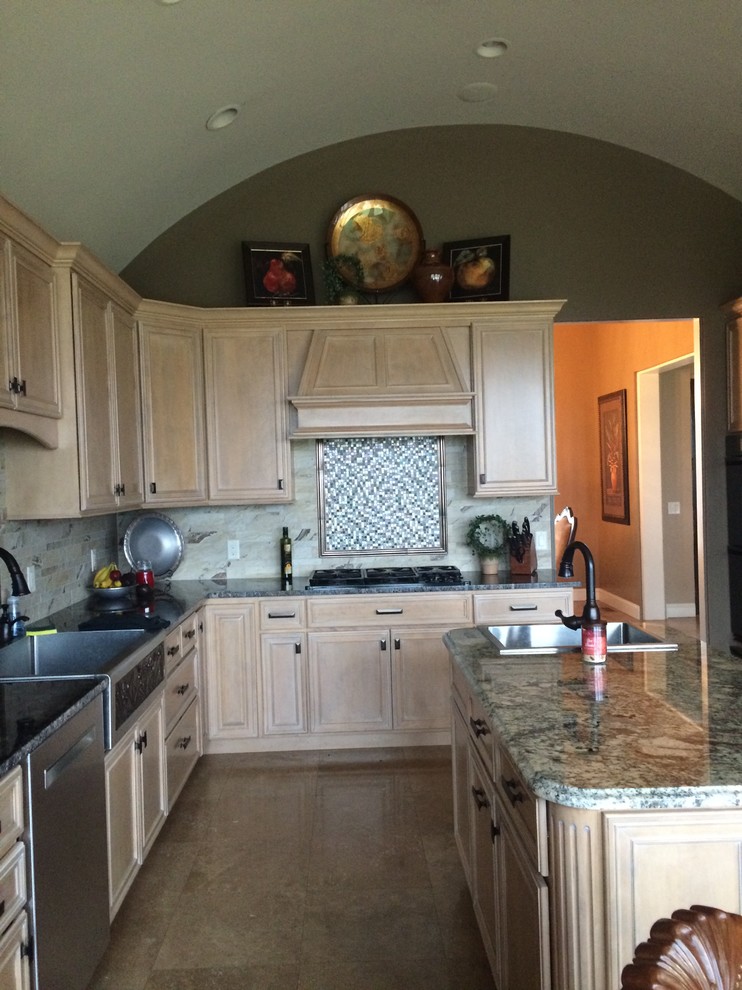 This is an example of a large mediterranean u-shaped kitchen in Other with a farmhouse sink, raised-panel cabinets, light wood cabinets, granite benchtops, grey splashback, ceramic splashback, stainless steel appliances, travertine floors and with island.