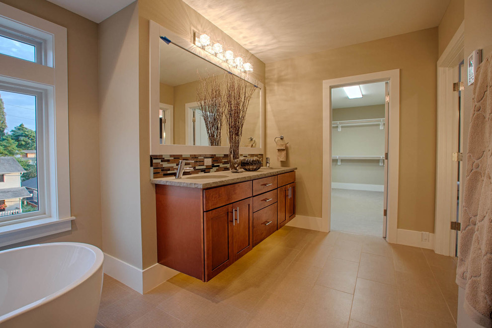 This is an example of a mid-sized contemporary master bathroom in Seattle with an undermount sink, shaker cabinets, medium wood cabinets, a freestanding tub, a one-piece toilet, beige tile, ceramic tile, beige walls and ceramic floors.