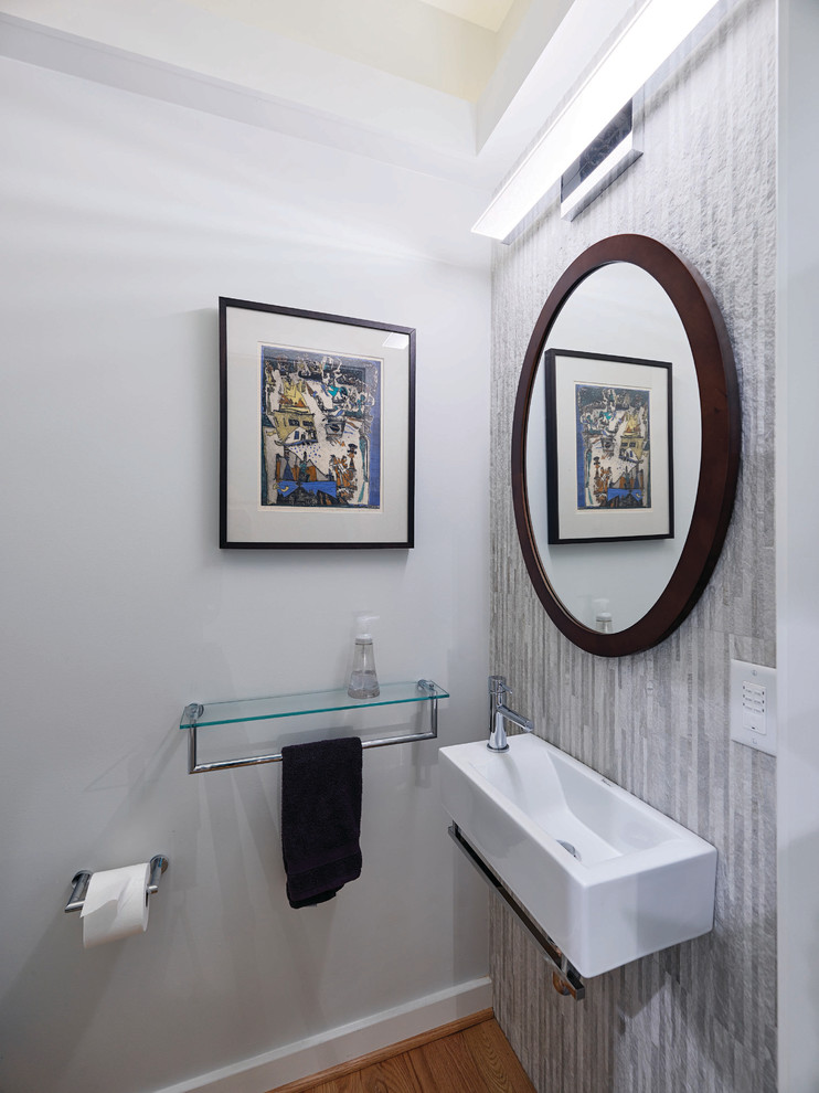 This is an example of a small modern powder room in Baltimore with a two-piece toilet, gray tile, porcelain tile, grey walls, light hardwood floors, a wall-mount sink, brown floor and white benchtops.