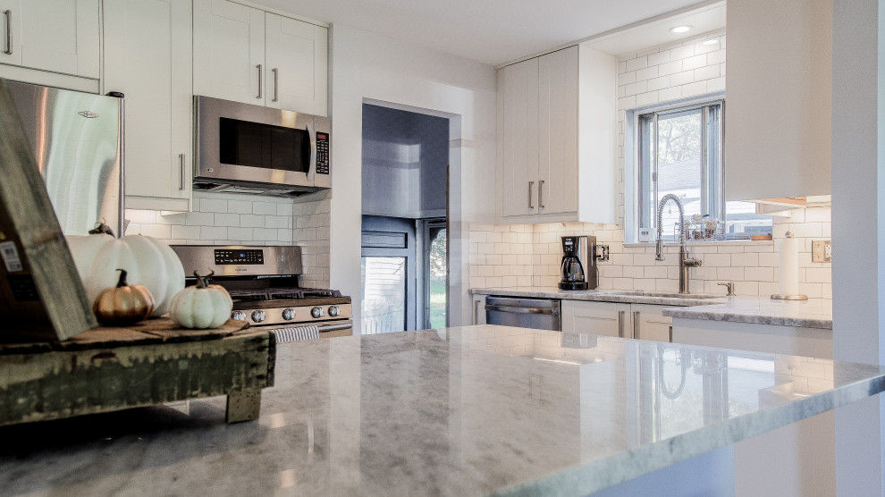 This is an example of a mid-sized country l-shaped eat-in kitchen in Detroit with an undermount sink, shaker cabinets, white cabinets, granite benchtops, white splashback, subway tile splashback, stainless steel appliances, ceramic floors, a peninsula, grey floor and grey benchtop.