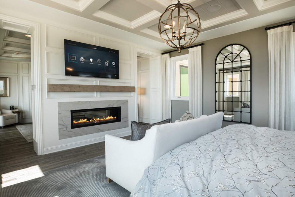 This is an example of a large traditional master bedroom in Los Angeles with grey walls, dark hardwood floors, a two-sided fireplace, a stone fireplace surround and grey floor.
