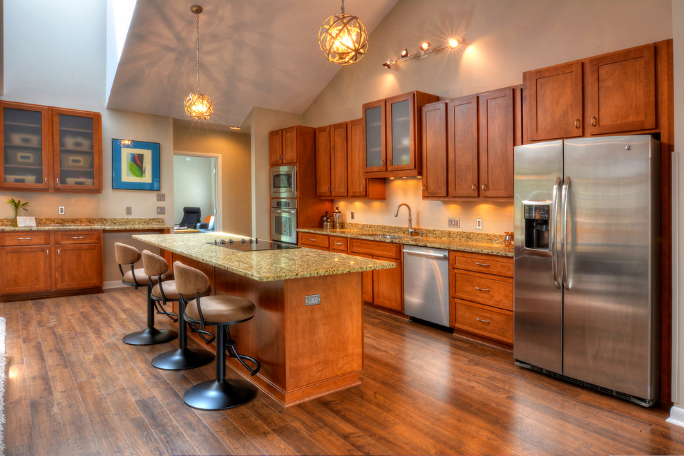 This is an example of a large transitional open plan kitchen in Charlotte with a double-bowl sink, raised-panel cabinets, brown cabinets, granite benchtops, beige splashback, stainless steel appliances, laminate floors and with island.