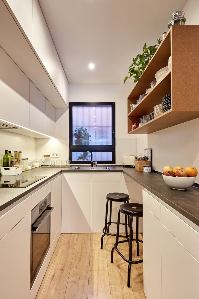 Design ideas for a small contemporary u-shaped separate kitchen in Other with a drop-in sink, flat-panel cabinets, white cabinets, white splashback, stainless steel appliances, light hardwood floors, beige floor and grey benchtop.