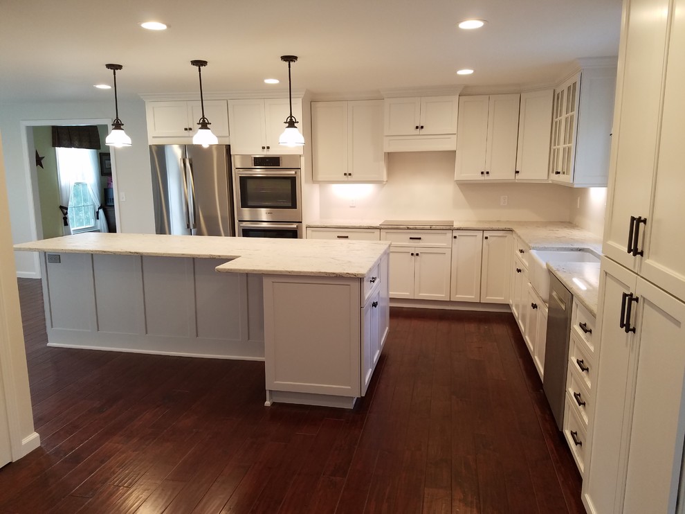 Inspiration for a mid-sized transitional l-shaped dark wood floor and brown floor eat-in kitchen remodel with a farmhouse sink, shaker cabinets, white cabinets, granite countertops, white backsplash, subway tile backsplash, stainless steel appliances and an island