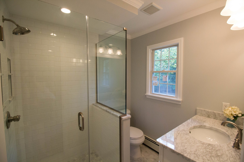 Photo of a small transitional master bathroom in Newark with shaker cabinets, white cabinets, a corner shower, a two-piece toilet, white tile, ceramic tile, grey walls, marble floors, an undermount sink, marble benchtops, grey floor and a hinged shower door.