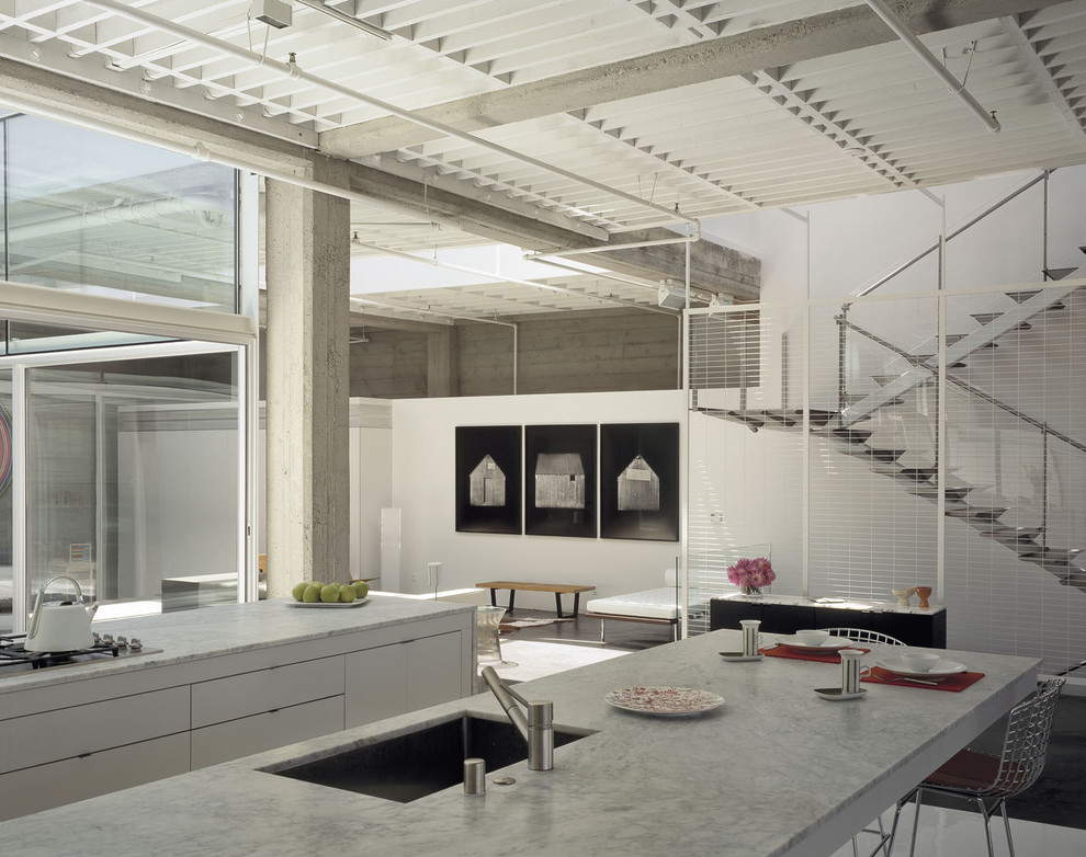 This is an example of a mid-sized industrial galley eat-in kitchen in San Francisco with an undermount sink, flat-panel cabinets, white cabinets, marble benchtops, stainless steel appliances, concrete floors, with island and grey floor.
