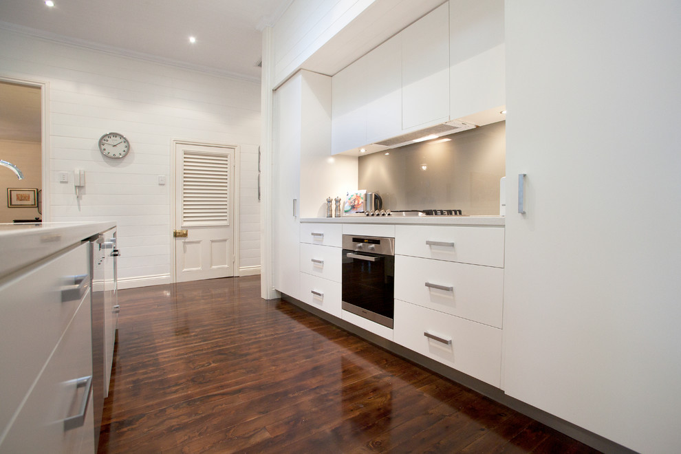 Design ideas for a large contemporary galley open plan kitchen in Brisbane with a double-bowl sink, flat-panel cabinets, white cabinets, quartz benchtops, grey splashback, glass sheet splashback, stainless steel appliances, dark hardwood floors and with island.