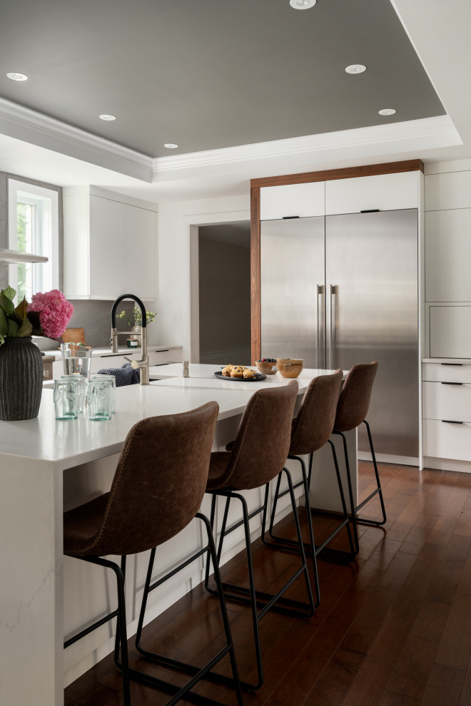 Inspiration for a large transitional u-shaped eat-in kitchen in Montreal with an undermount sink, flat-panel cabinets, white cabinets, quartz benchtops, grey splashback, slate splashback, stainless steel appliances, dark hardwood floors, with island, brown floor, white benchtop and coffered.