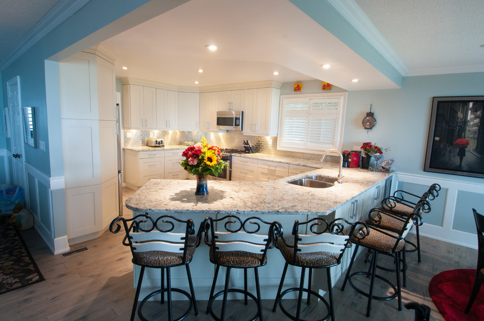 Large transitional u-shaped light wood floor open concept kitchen photo in Toronto with a double-bowl sink, shaker cabinets, white cabinets, quartzite countertops, gray backsplash, subway tile backsplash, stainless steel appliances and a peninsula