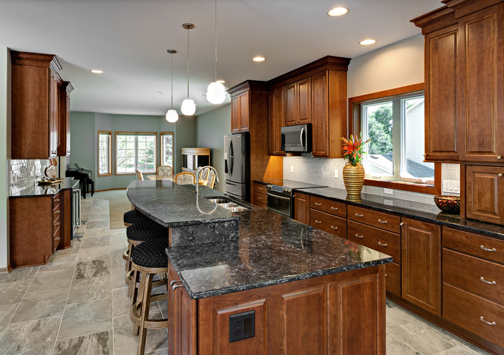 Photo of a large traditional galley eat-in kitchen in Minneapolis with a triple-bowl sink, raised-panel cabinets, medium wood cabinets, quartz benchtops, grey splashback, cement tile splashback, stainless steel appliances, porcelain floors, with island, grey floor and grey benchtop.