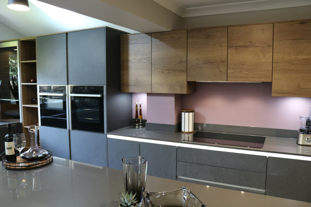 Design ideas for a large contemporary l-shaped eat-in kitchen in Sussex with an undermount sink, flat-panel cabinets, grey cabinets, quartzite benchtops, grey splashback, glass sheet splashback, black appliances, vinyl floors, with island, beige floor and grey benchtop.