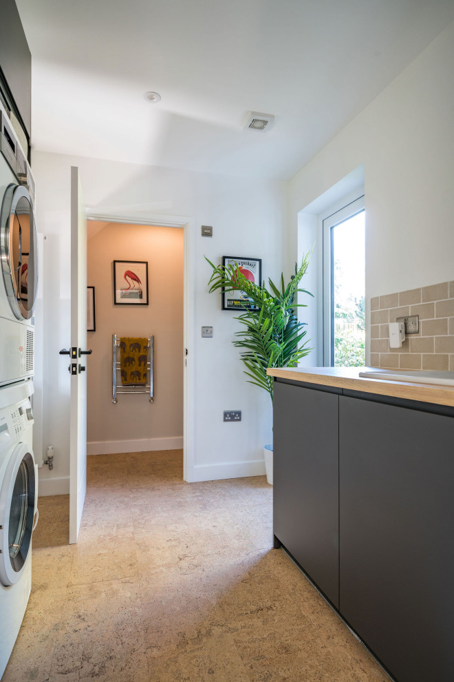 This is an example of a mid-sized modern galley dedicated laundry room in Oxfordshire with an integrated sink, flat-panel cabinets, grey cabinets, wood benchtops, beige splashback, ceramic splashback, white walls, cork floors, beige floor and beige benchtop.