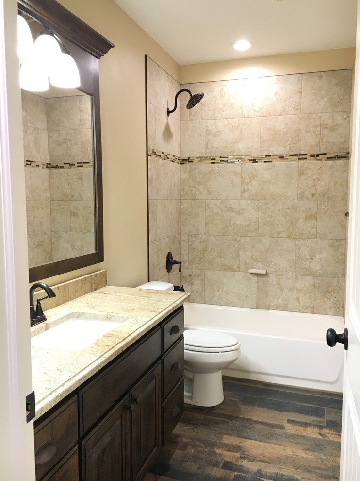 Mid-sized transitional kids' beige tile and porcelain tile porcelain tile alcove bathtub photo with raised-panel cabinets, dark wood cabinets, a two-piece toilet, beige walls, an undermount sink and granite countertops