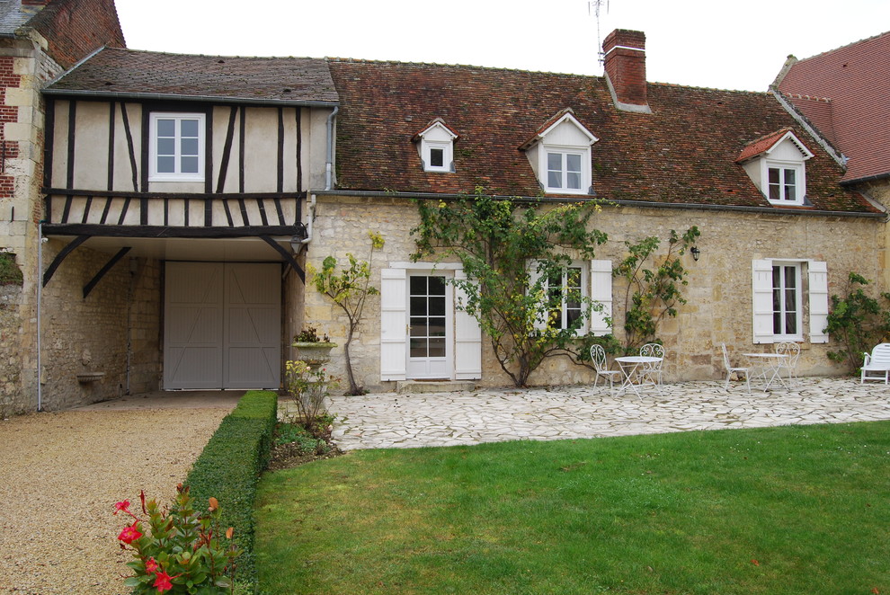 Large country two-storey beige exterior in Paris with stone veneer and a gable roof.