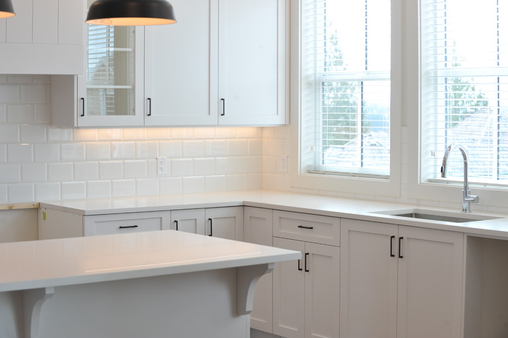 Photo of a contemporary eat-in kitchen in Vancouver with a single-bowl sink, shaker cabinets, white cabinets, white splashback, subway tile splashback, medium hardwood floors, with island and brown floor.