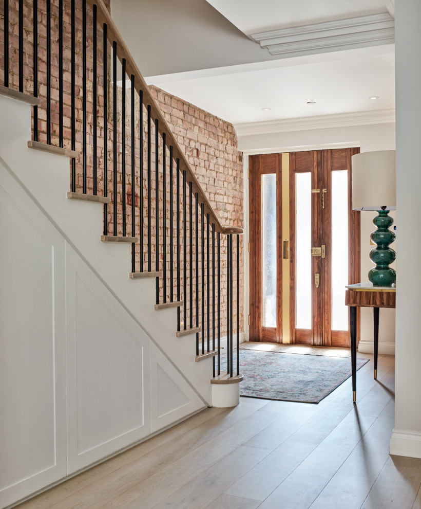 This is an example of a mid-sized transitional wood straight staircase in London with metal railing and brick walls.