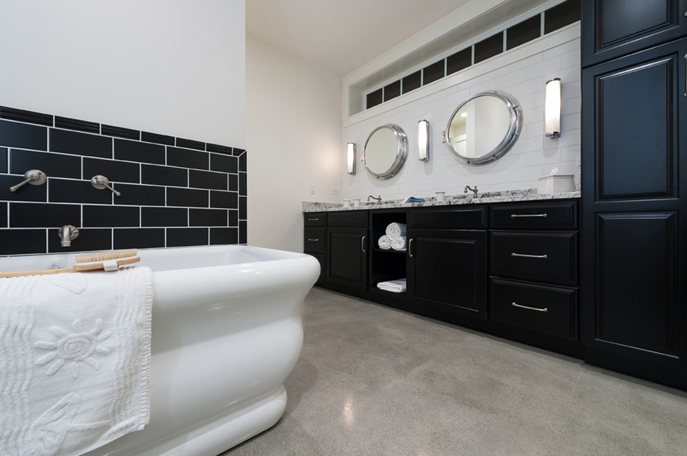 Inspiration for a beach style master bathroom in San Diego with an undermount sink, raised-panel cabinets, black cabinets, granite benchtops, a freestanding tub, black tile, ceramic tile and concrete floors.