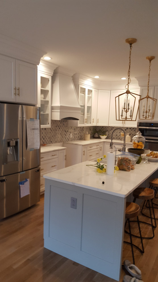 Example of a large transitional u-shaped light wood floor and brown floor eat-in kitchen design in DC Metro with a farmhouse sink, recessed-panel cabinets, white cabinets, quartzite countertops, gray backsplash, marble backsplash, stainless steel appliances, an island and white countertops