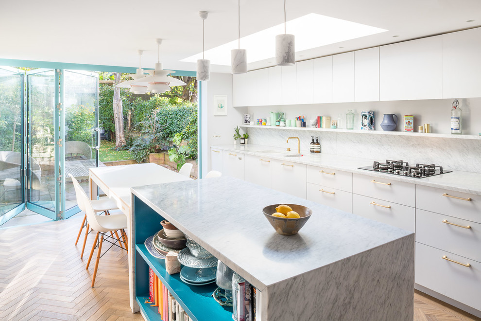 Contemporary single-wall eat-in kitchen in London with a drop-in sink, flat-panel cabinets, white cabinets, marble benchtops, white splashback, marble splashback, stainless steel appliances, medium hardwood floors, with island and brown floor.