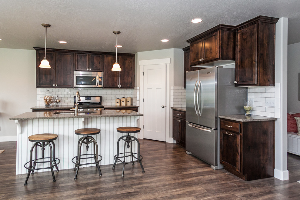 Large industrial single-wall eat-in kitchen in Salt Lake City with a drop-in sink, dark wood cabinets, white splashback, stainless steel appliances, dark hardwood floors, with island, shaker cabinets, granite benchtops, subway tile splashback and brown floor.