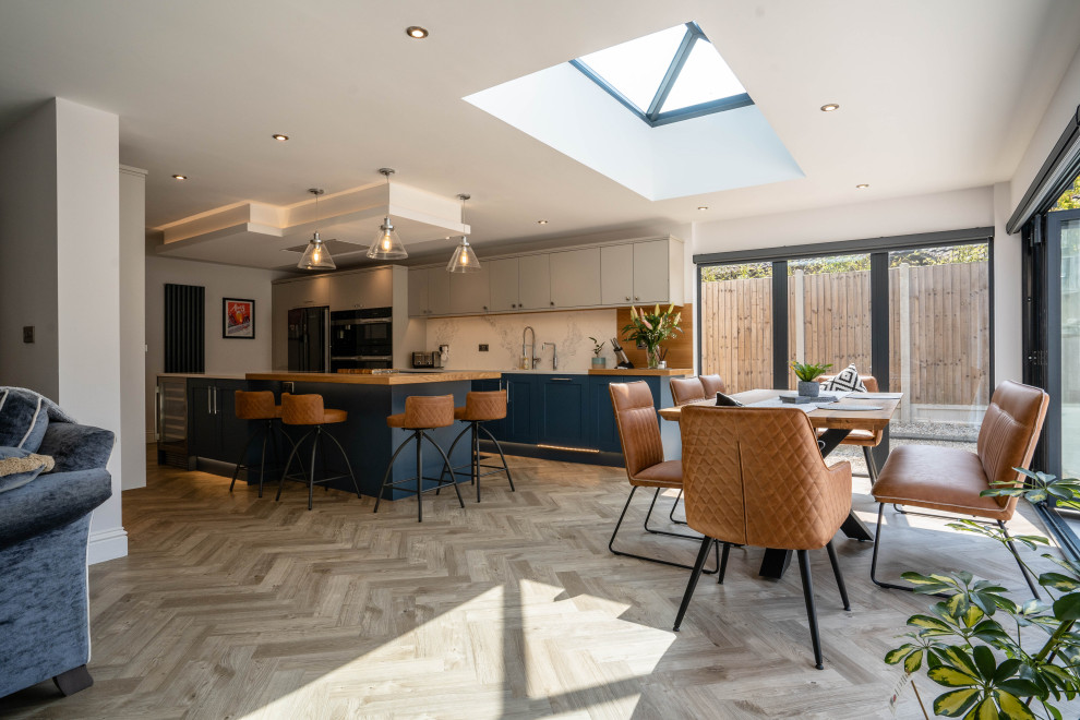 Photo of a large modern u-shaped open plan kitchen in Essex with an integrated sink, shaker cabinets, blue cabinets, quartzite benchtops, white splashback, engineered quartz splashback, panelled appliances, with island and white benchtop.