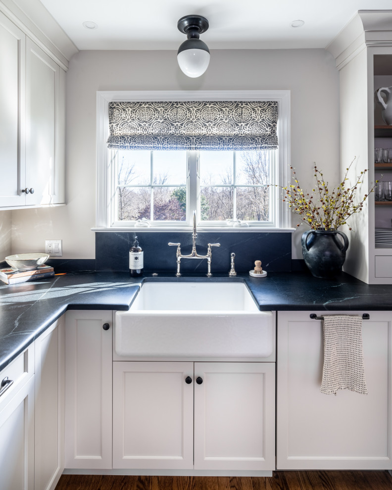 This is an example of a medium sized classic l-shaped kitchen/diner in Philadelphia with a belfast sink, shaker cabinets, grey cabinets, soapstone worktops, black splashback, stone slab splashback, stainless steel appliances, medium hardwood flooring, an island, brown floors and black worktops.