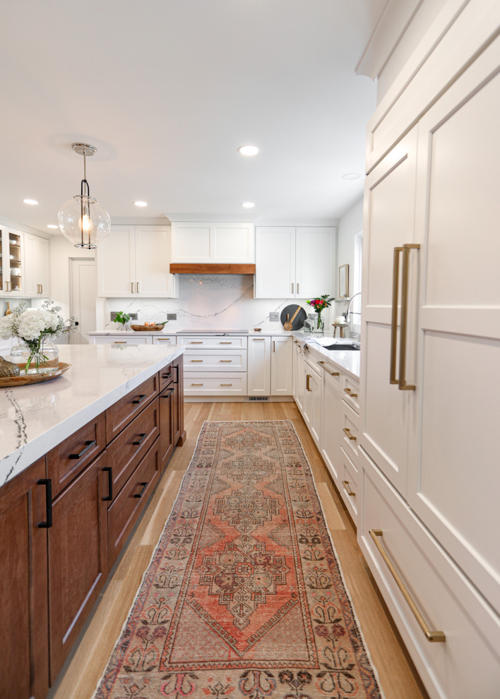 Inspiration for a large transitional u-shaped eat-in kitchen in Chicago with an undermount sink, shaker cabinets, white cabinets, quartz benchtops, beige splashback, engineered quartz splashback, panelled appliances, light hardwood floors, with island and white benchtop.