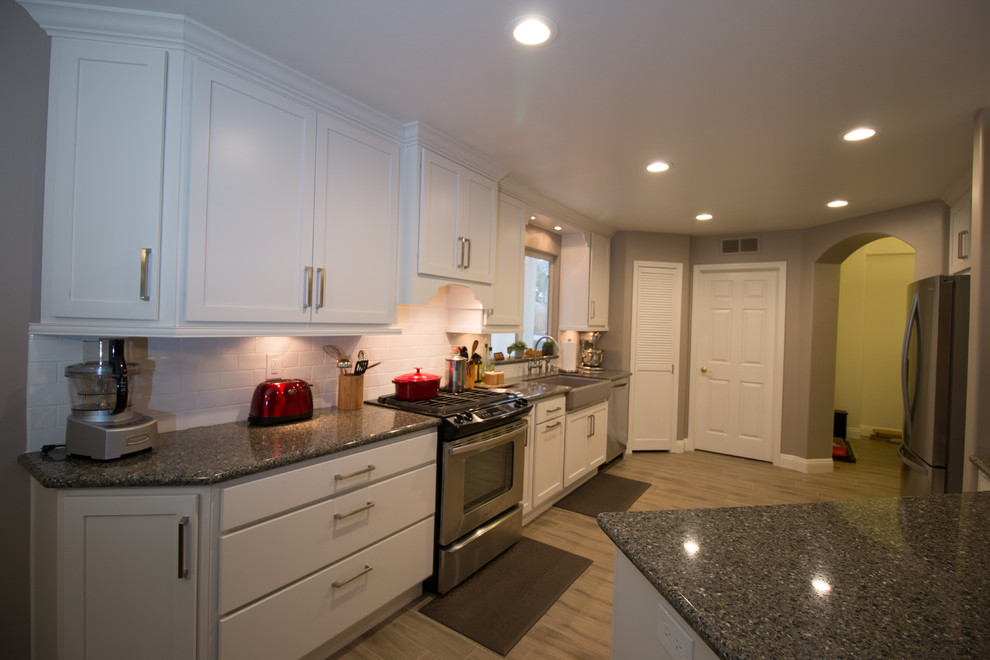 Mid-sized transitional galley porcelain tile open concept kitchen photo with a farmhouse sink, shaker cabinets, white cabinets, quartz countertops, white backsplash, subway tile backsplash and stainless steel appliances