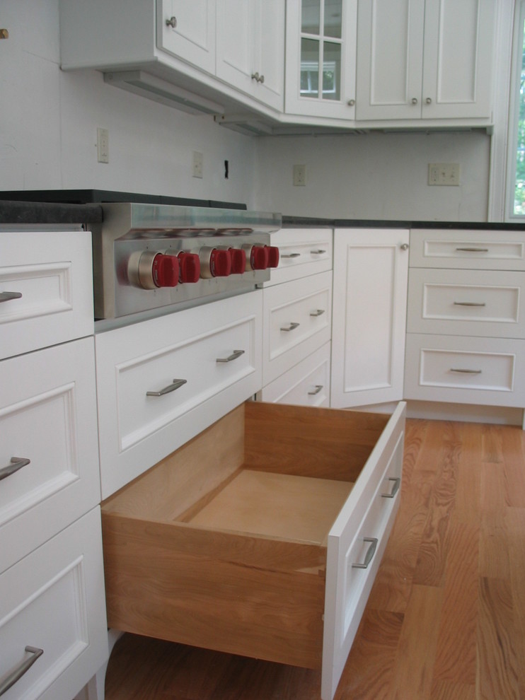 Inspiration for a mid-sized transitional l-shaped kitchen in Boston with a farmhouse sink, recessed-panel cabinets, white cabinets, solid surface benchtops, white splashback, marble splashback, stainless steel appliances, medium hardwood floors, multiple islands, brown floor and beige benchtop.