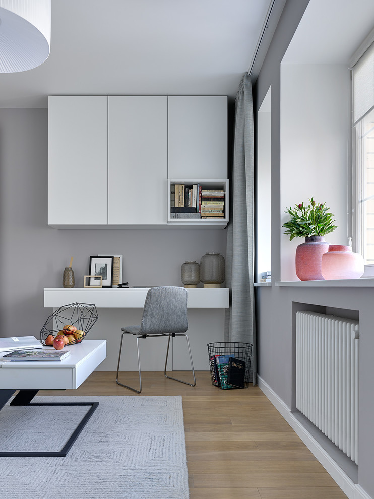 This is an example of a contemporary study room in Moscow with grey walls, light hardwood floors and a built-in desk.