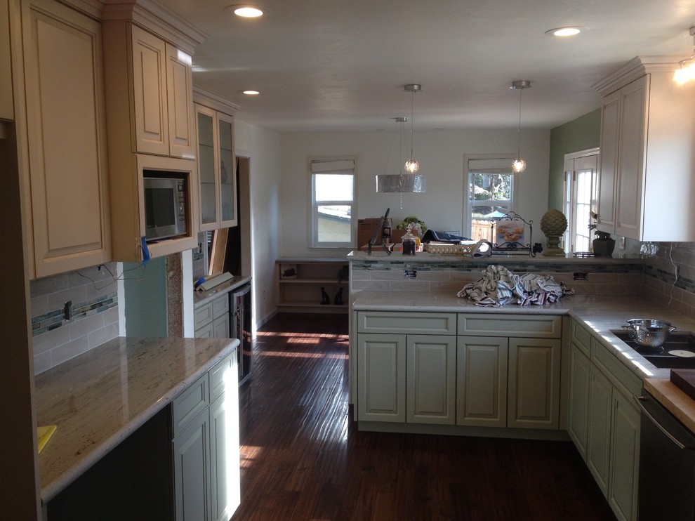 Photo of a mid-sized modern l-shaped eat-in kitchen in San Francisco with an undermount sink, raised-panel cabinets, green cabinets, granite benchtops, beige splashback, subway tile splashback, stainless steel appliances, dark hardwood floors and a peninsula.