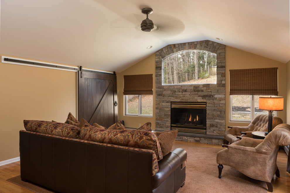 This is an example of a mid-sized arts and crafts open concept family room in Boston with a game room, beige walls, medium hardwood floors, a standard fireplace, a stone fireplace surround and a concealed tv.