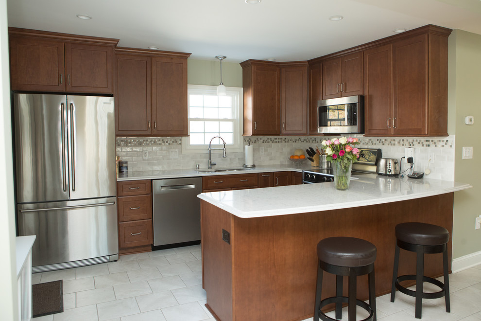 Mid-sized transitional l-shaped white floor and ceramic tile eat-in kitchen photo with an undermount sink, shaker cabinets, medium tone wood cabinets, white backsplash, stainless steel appliances, a peninsula, white countertops, quartz countertops and porcelain backsplash